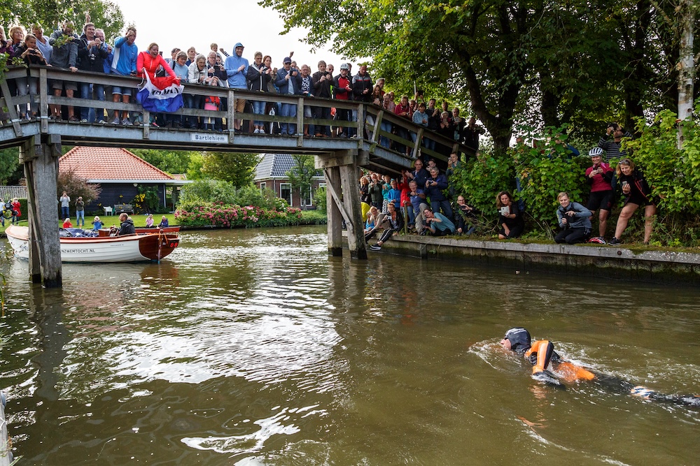Maarten van der Weijden zwemt door grachten met een hoop publiek dat hem aanmoedigt.